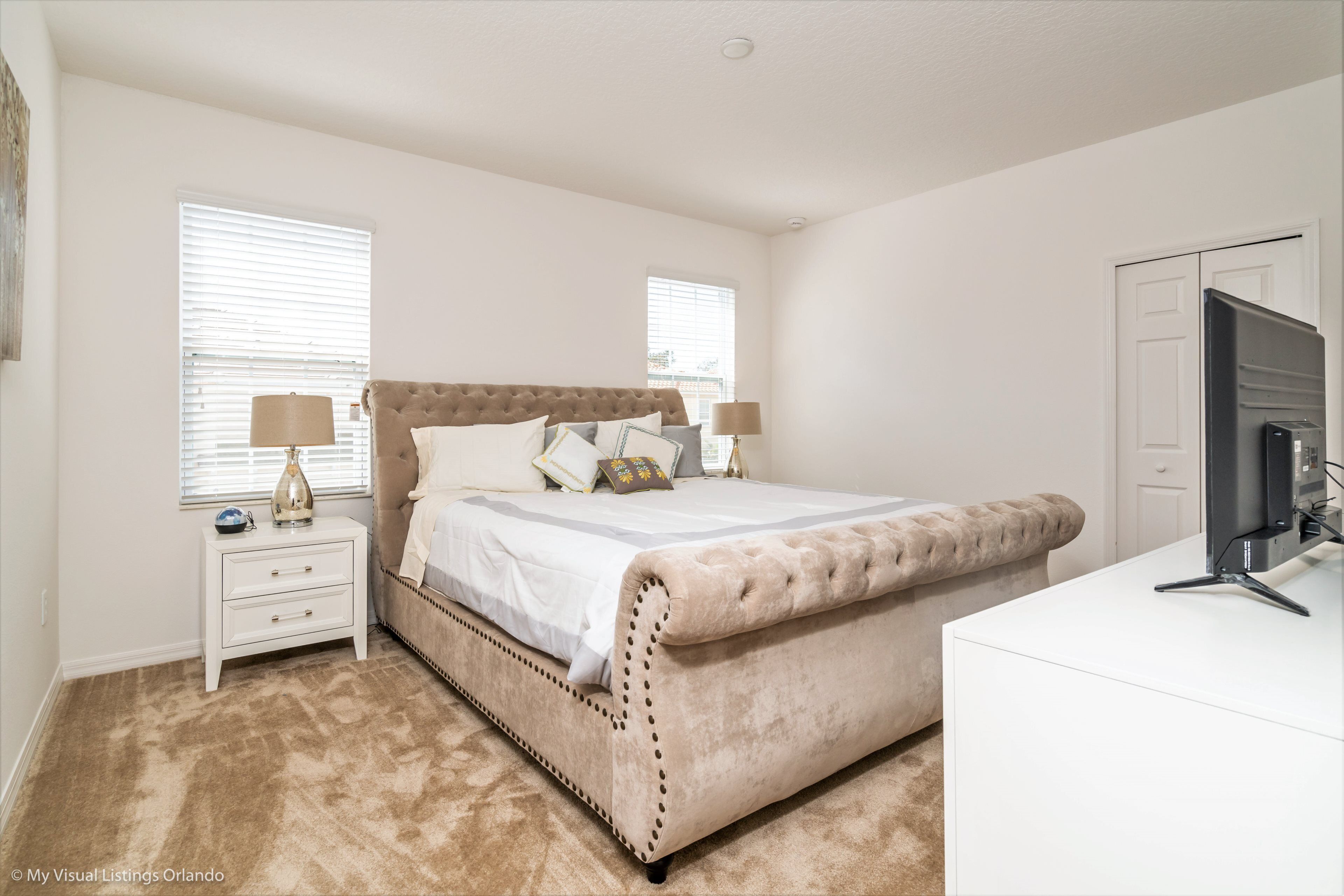 A bedroom with a large bed, a nightstand, a dresser, and a television.
