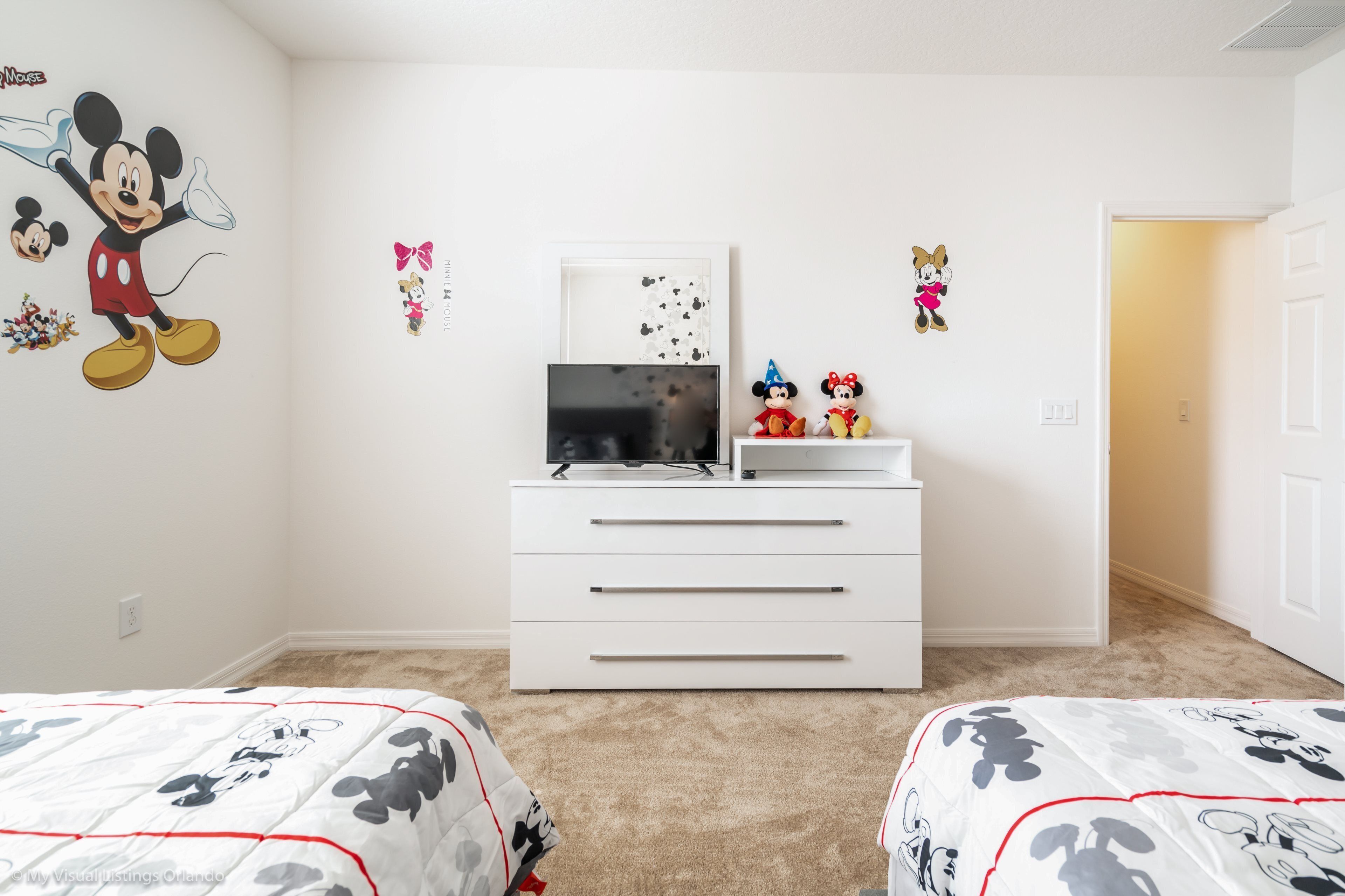 A bedroom with two beds, a white dresser, a TV, and Mickey Mouse decorations.