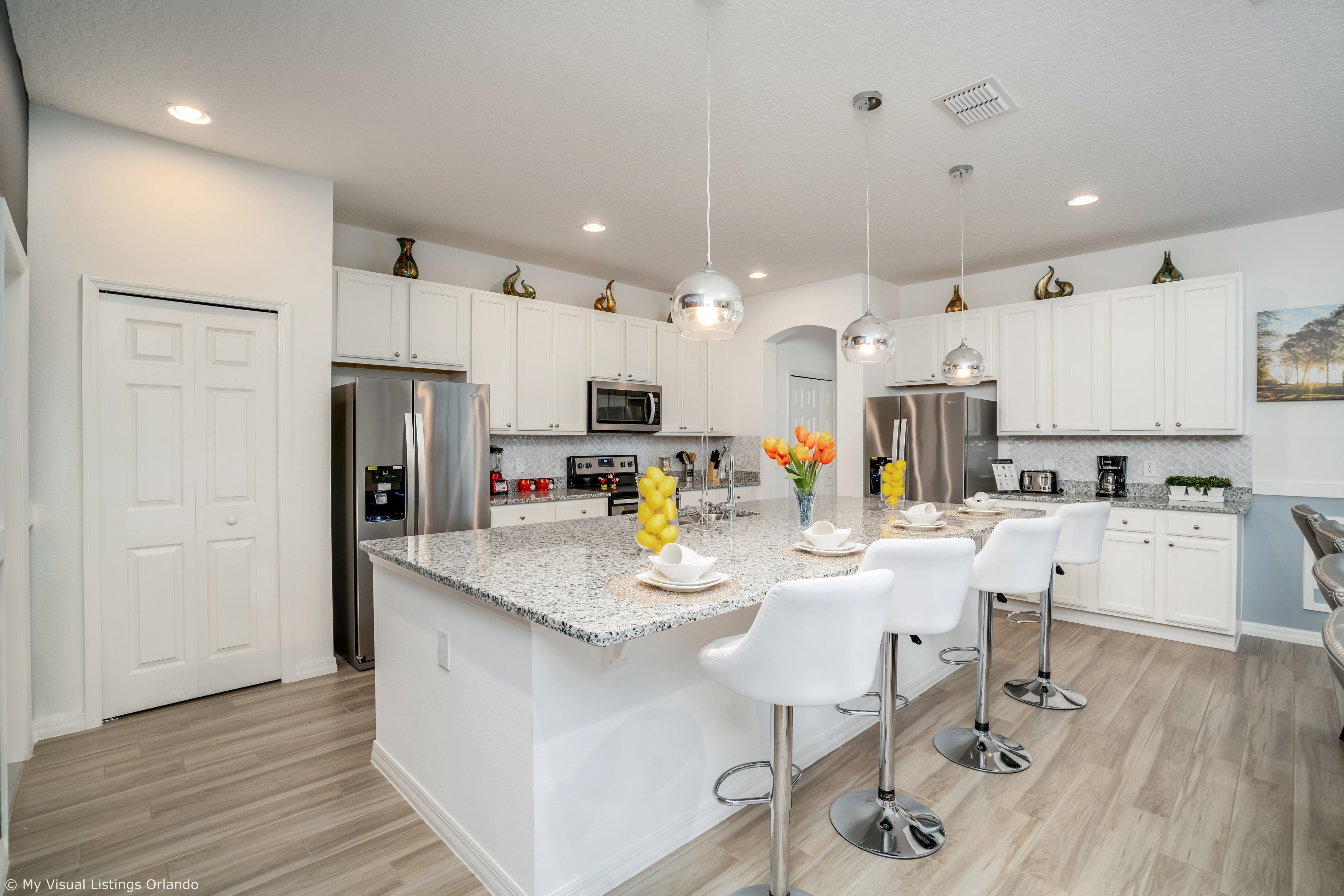 A modern kitchen with white cabinets, stainless steel appliances, a granite countertop, and a central island with bar stools.