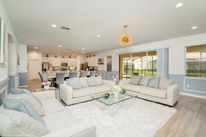 A spacious living area with a sofa set, a glass coffee table, and a modern chandelier.