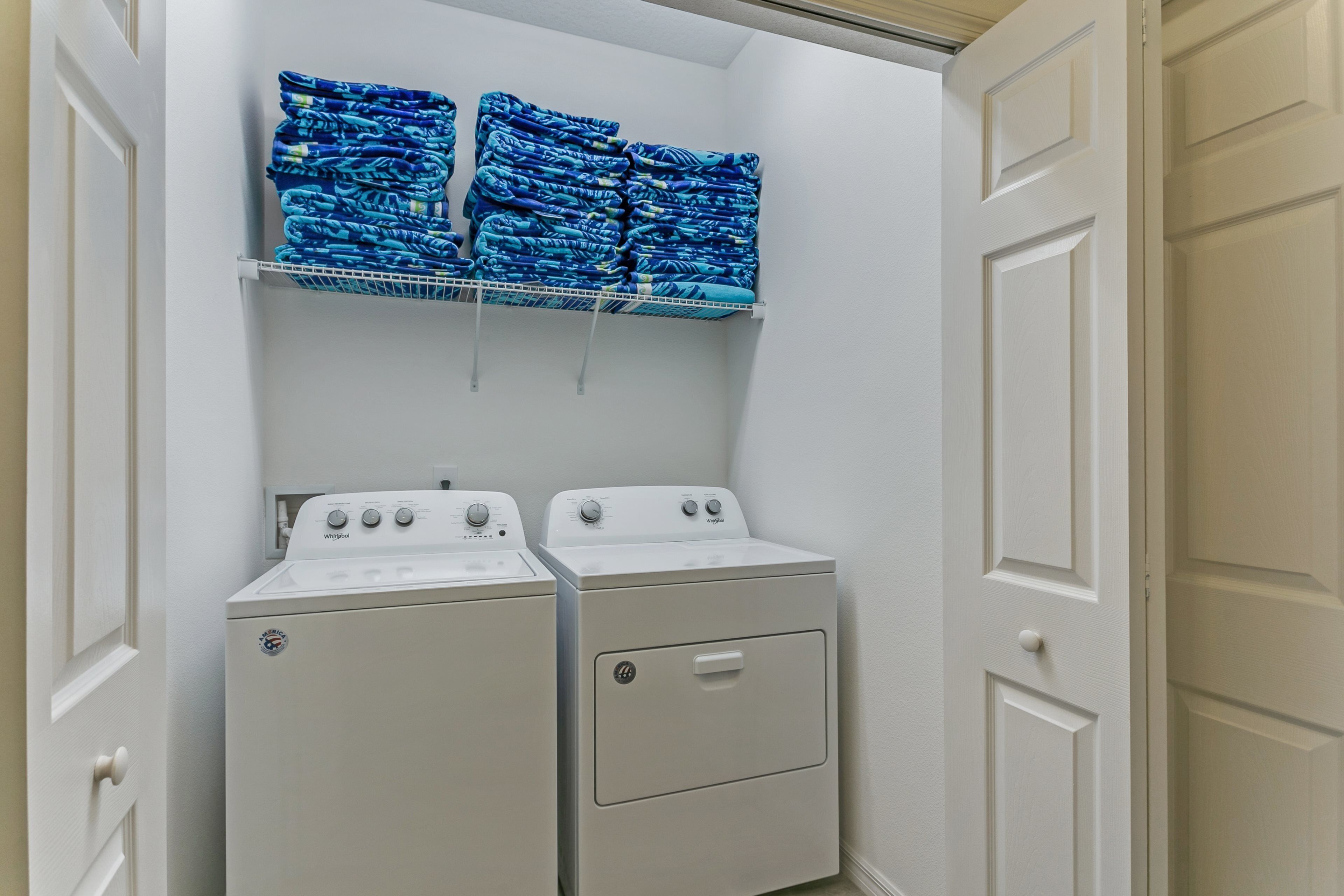 A laundry room with two stacked dryers and a shelf above holding folded blue blankets.