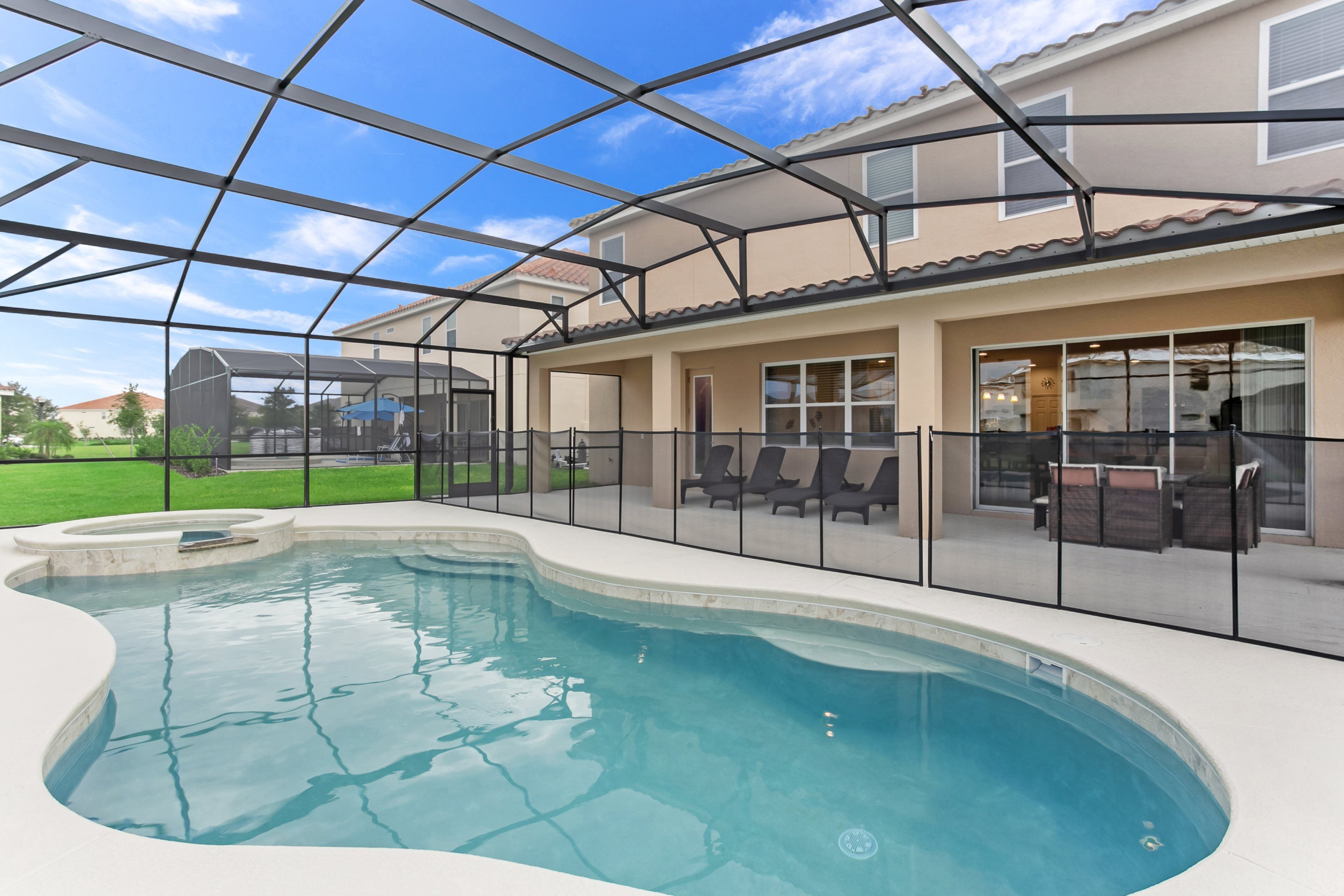 A swimming pool with a glass enclosure, outdoor seating, and a house in the background.