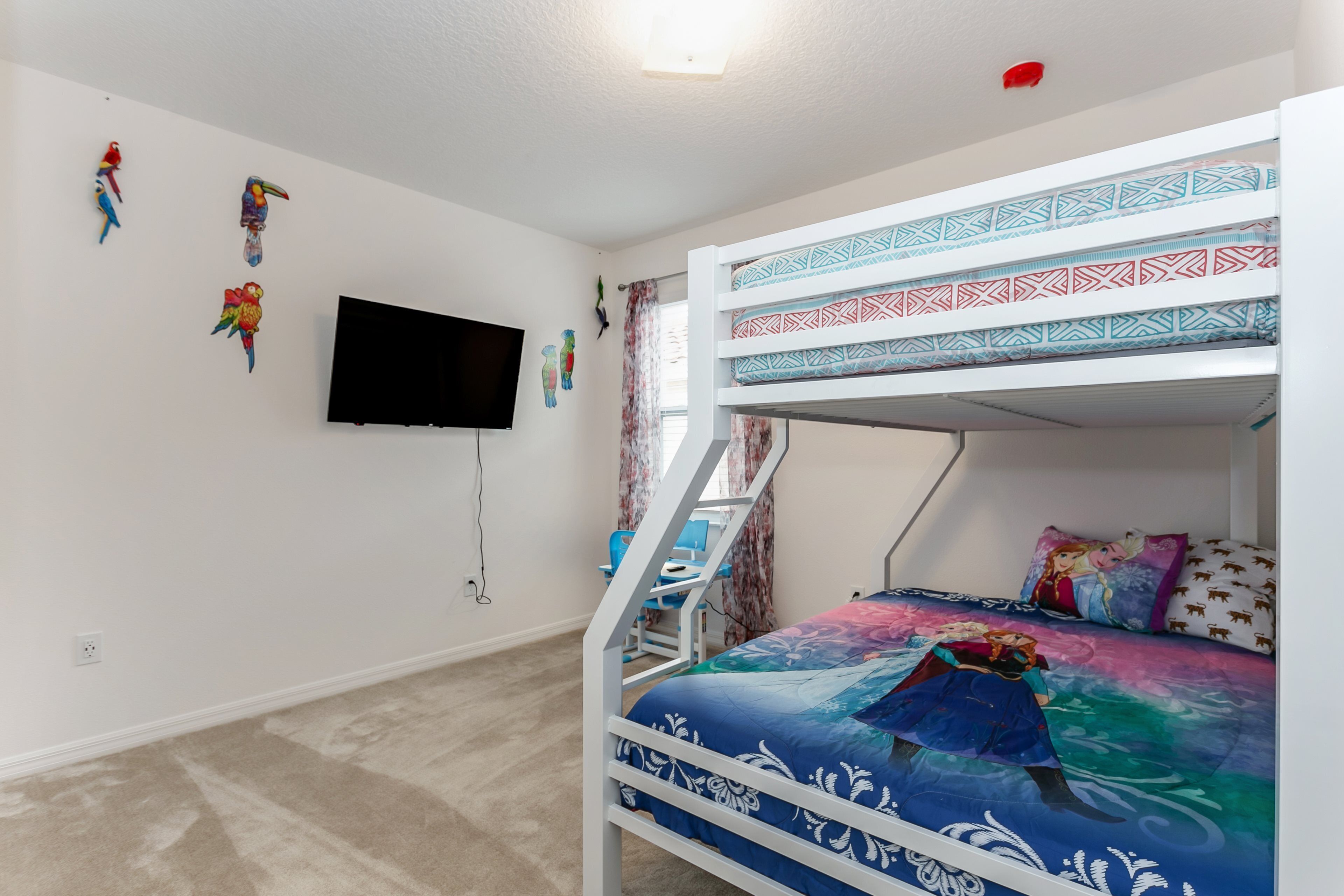 A bunk bed with a colorful bedspread, a desk with a chair, and a wall-mounted TV.