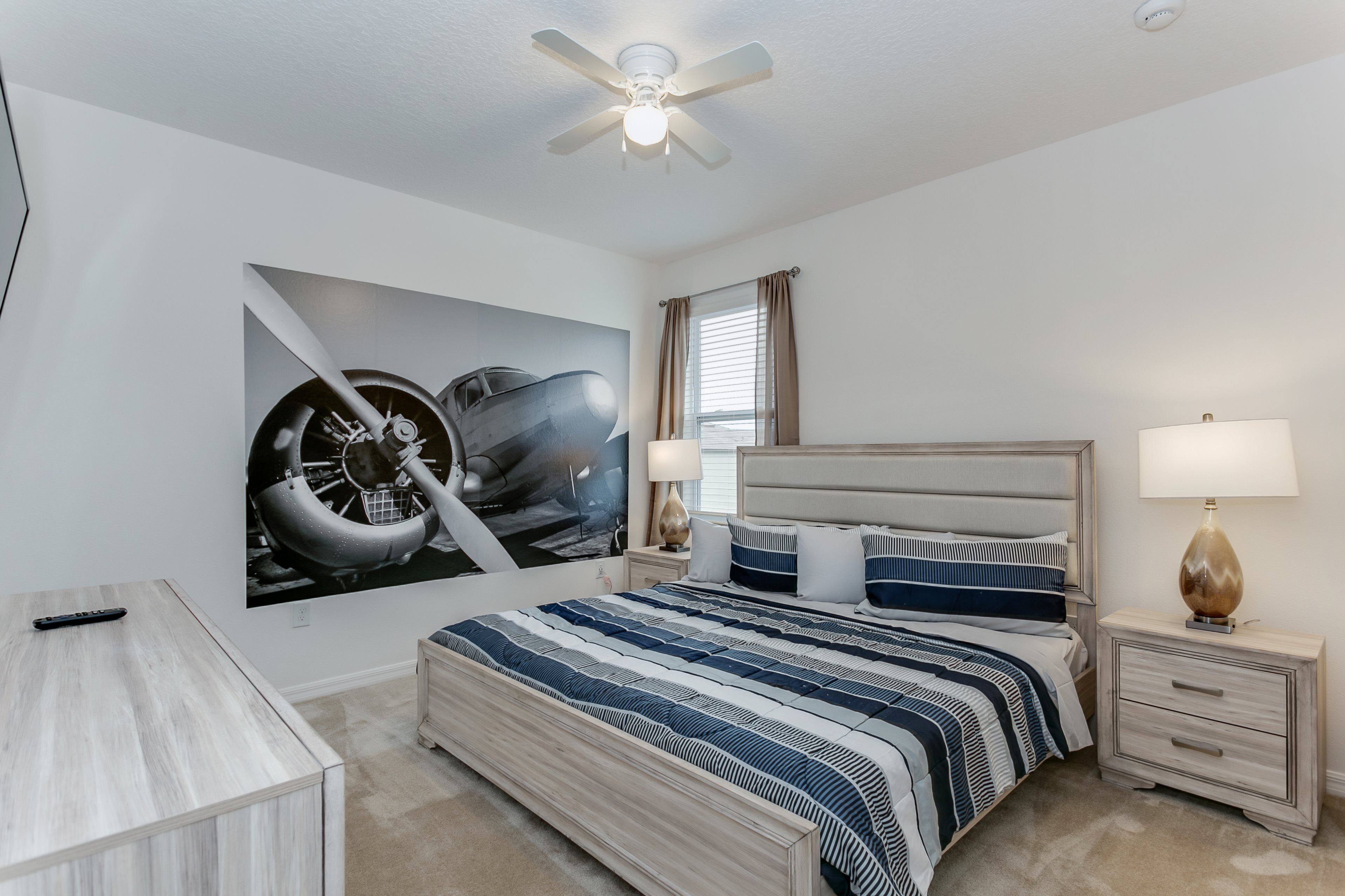 Ein Schlafzimmer mit Bett, Nachttischen, Schreibtisch, Deckenventilator und einem großen Wandbild.