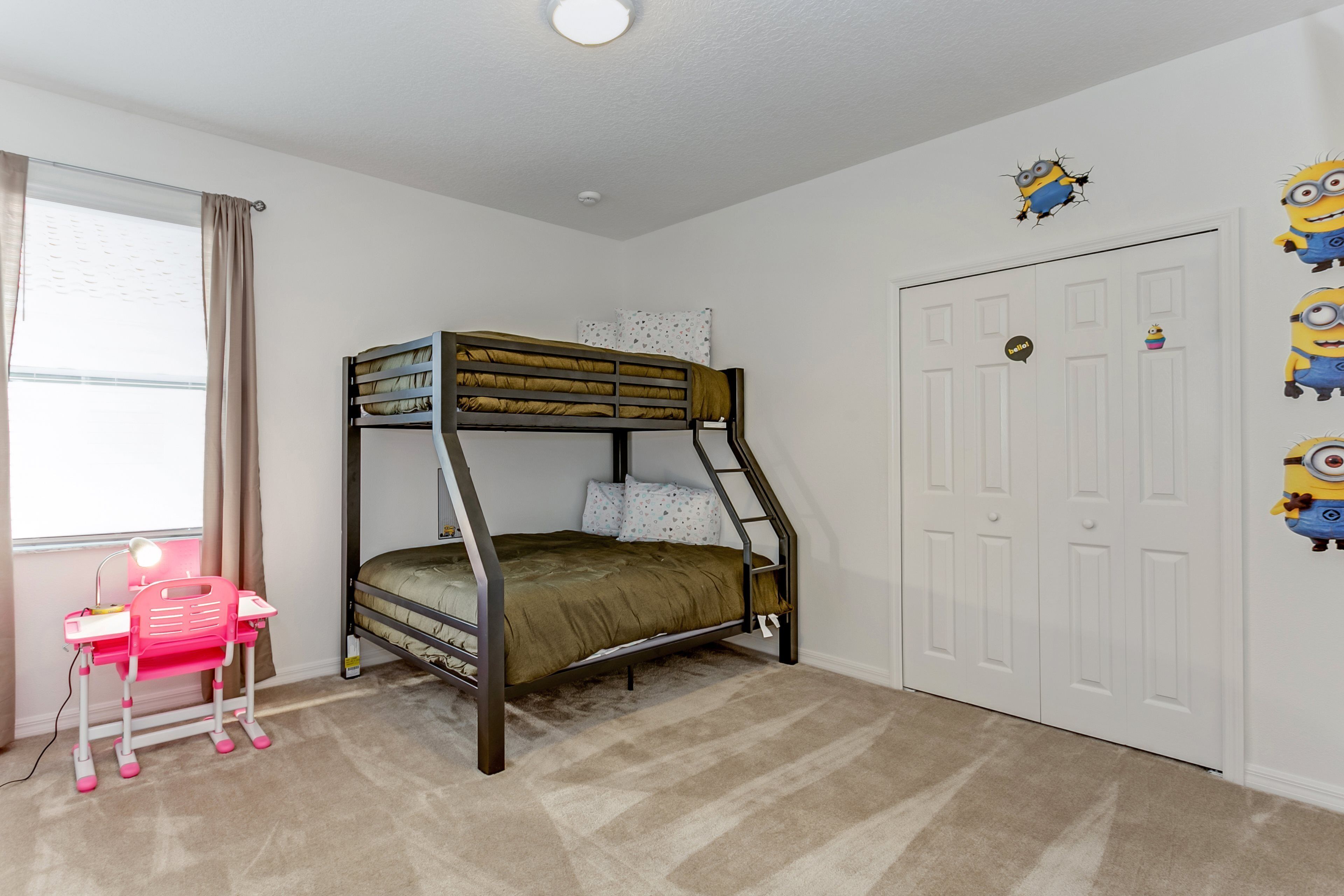 A bunk bed with a desk and chair, a window with curtains, and Minion wall decals.