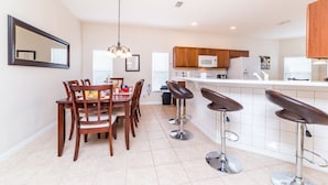 A modern kitchen with a dining area, featuring a large island with bar stools, wooden cabinets, and a hanging light fixture. - 170ed (Davenport)