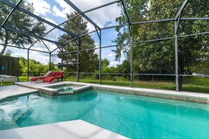 Ein Schwimmbad mit Glasveranda, roten Liegestühlen und einem Whirlpool.