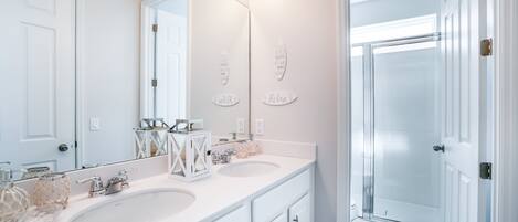 A bathroom with two sinks, a large mirror, and a glass shower enclosure.