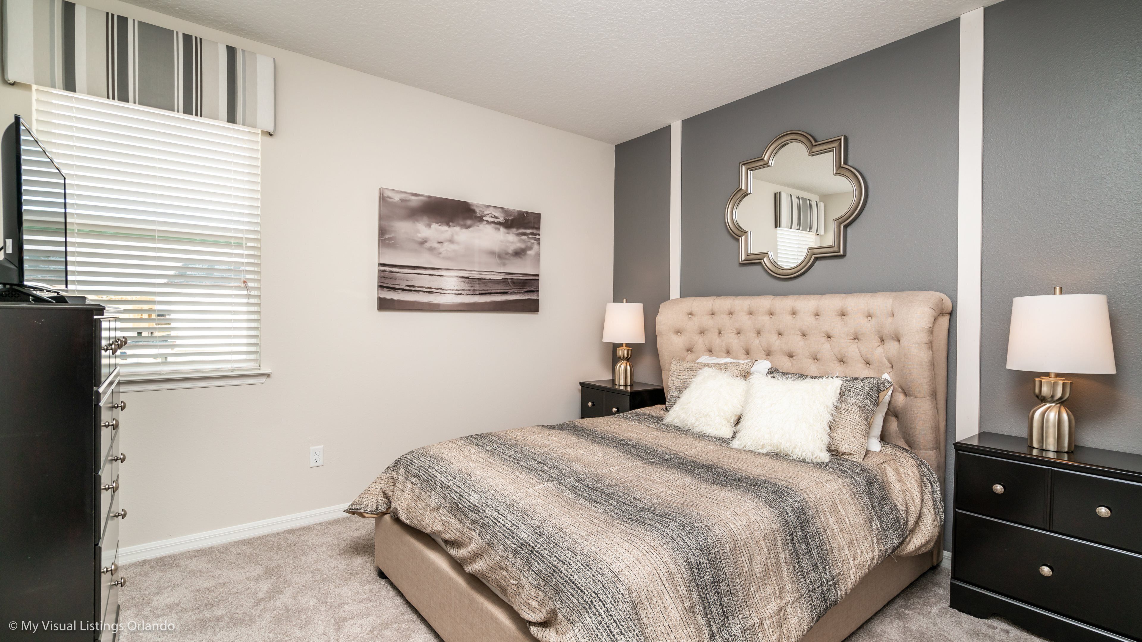 A bedroom with a tufted headboard, two bedside tables with lamps, a large mirror, and a painting on the wall.