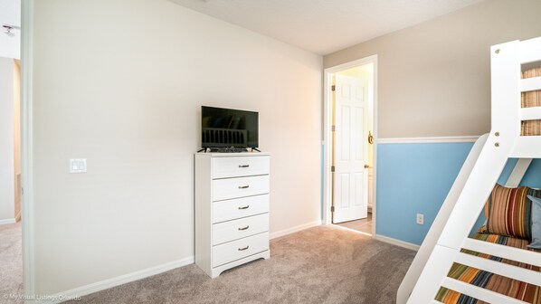 A bedroom with a white dresser, a television on top, a door leading to another room, and a bunk bed with striped bedding.