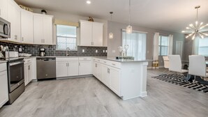 A modern kitchen with white cabinets, a central island, stainless steel appliances, and pendant lighting. - 6 Bed 5 Ba Villa with Games, Pool & Spa (Davenport)