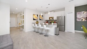 A modern kitchen with white bar stools, a central island, and stainless steel appliances. - 4832ds (Kissimmee)