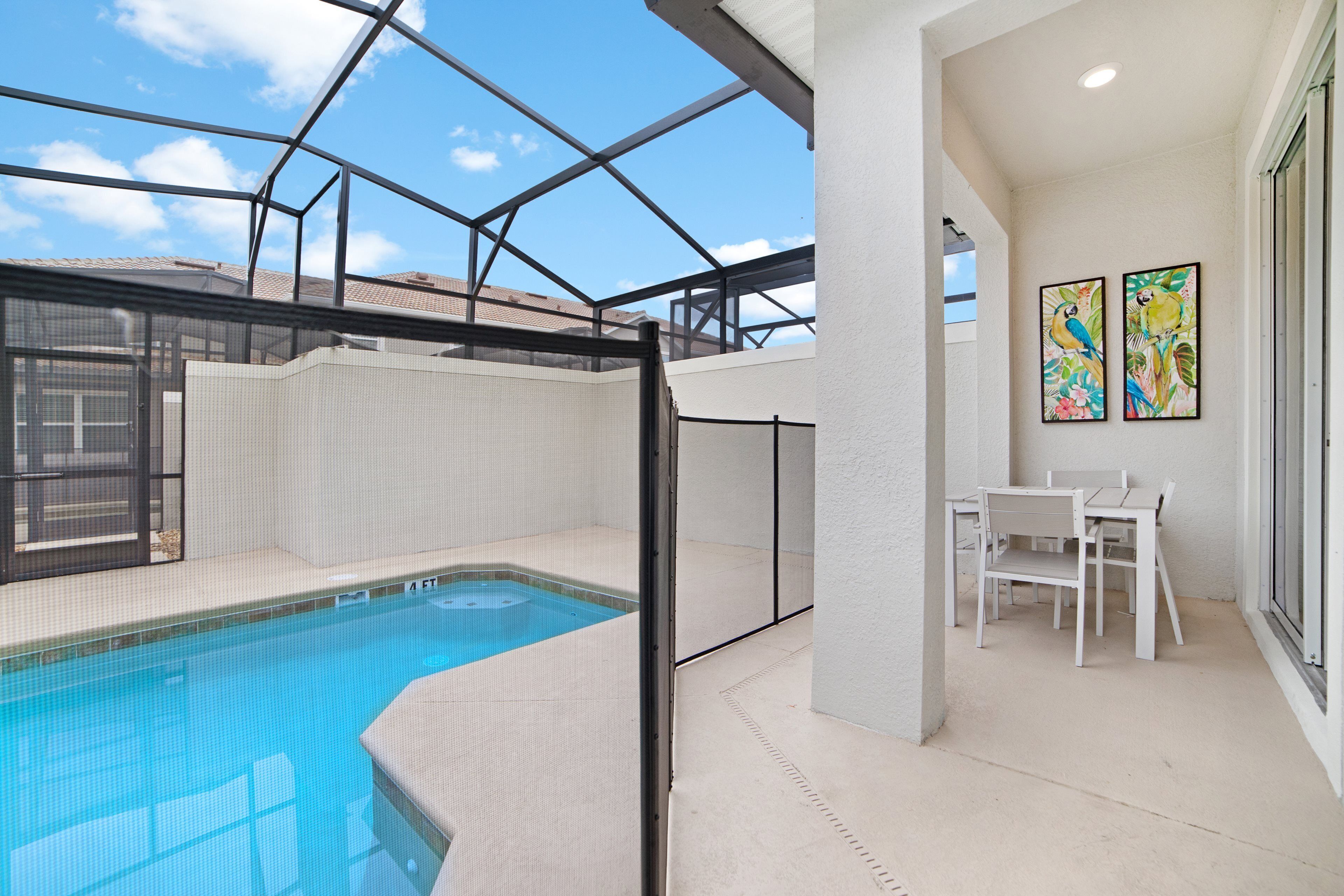 A rooftop pool area with a glass enclosure, a seating area with chairs, and two framed artworks on the wall.