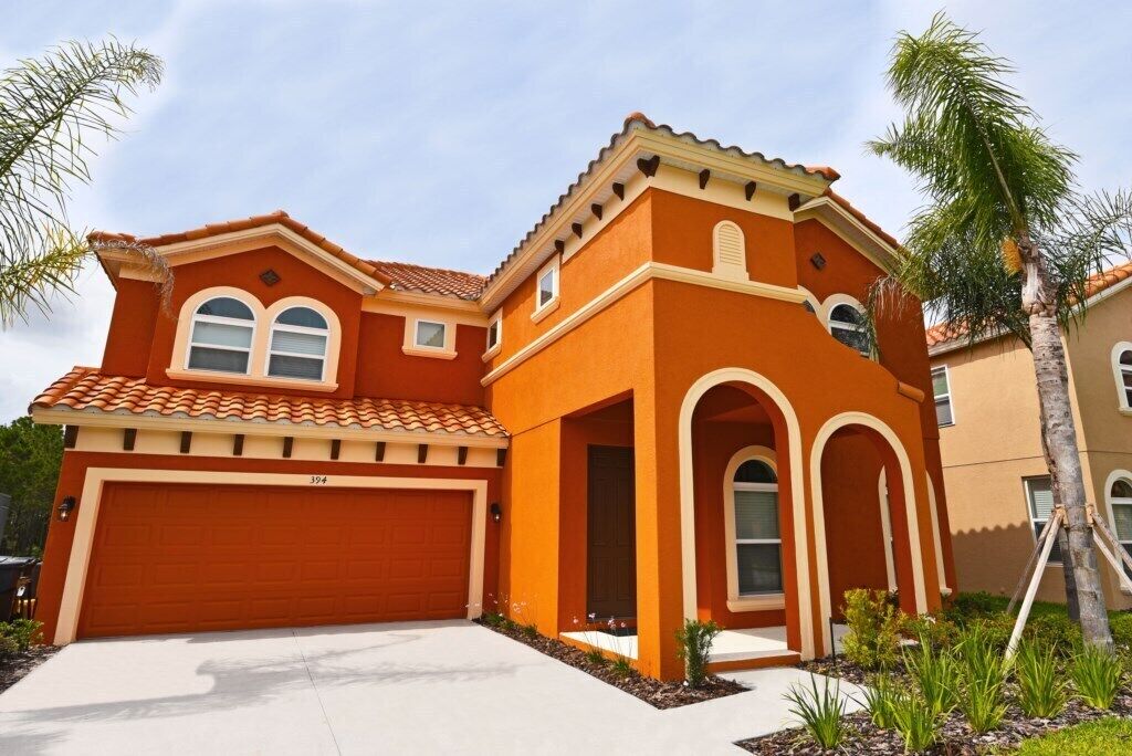 A two-story house with a red garage, a small porch with columns, and a tiled roof.
