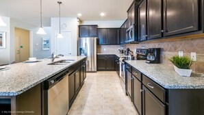 A modern kitchen with dark cabinets, stainless steel appliances, granite countertops, and pendant lighting. - Beautiful 8 Bed Villa Pool & Spa (Kissimmee)