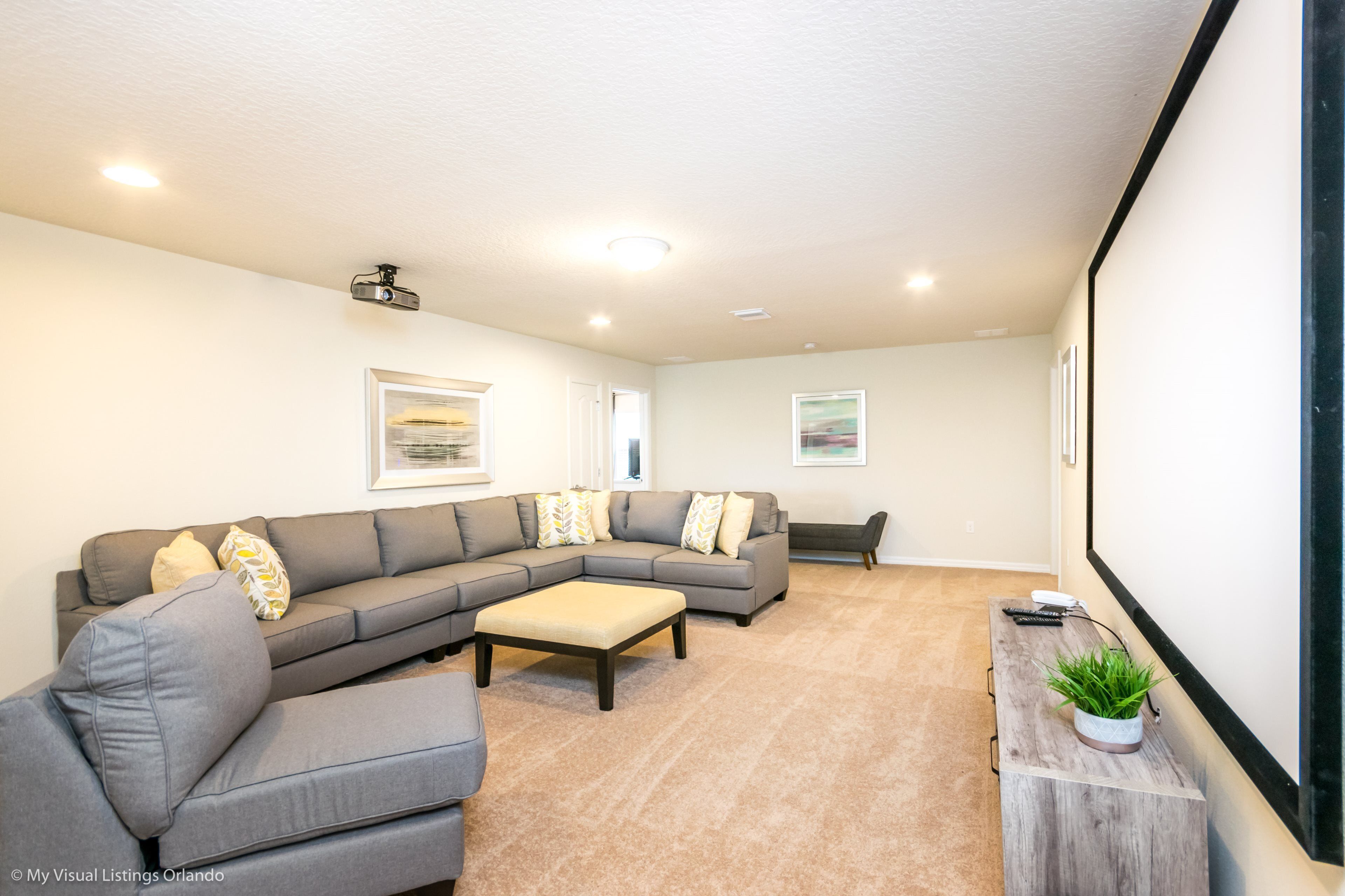 A living room with a sectional sofa, ottoman, and a flat-screen TV mounted on the wall.