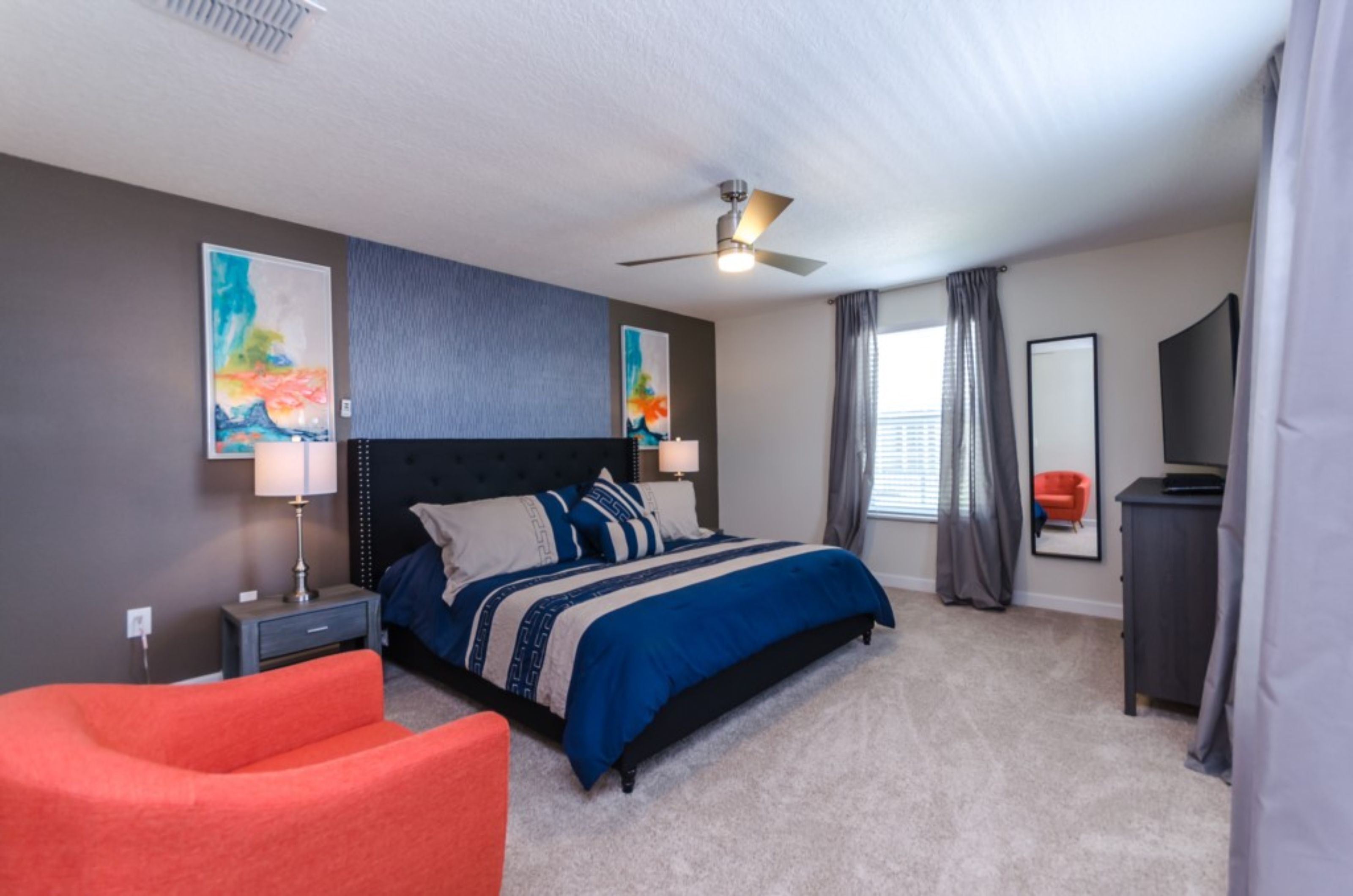 A bedroom with a bed, a nightstand, a chair, a ceiling fan, and artwork on the walls.