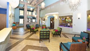 A spacious lobby with a high ceiling, wooden beams, and a central seating area with colorful chairs.