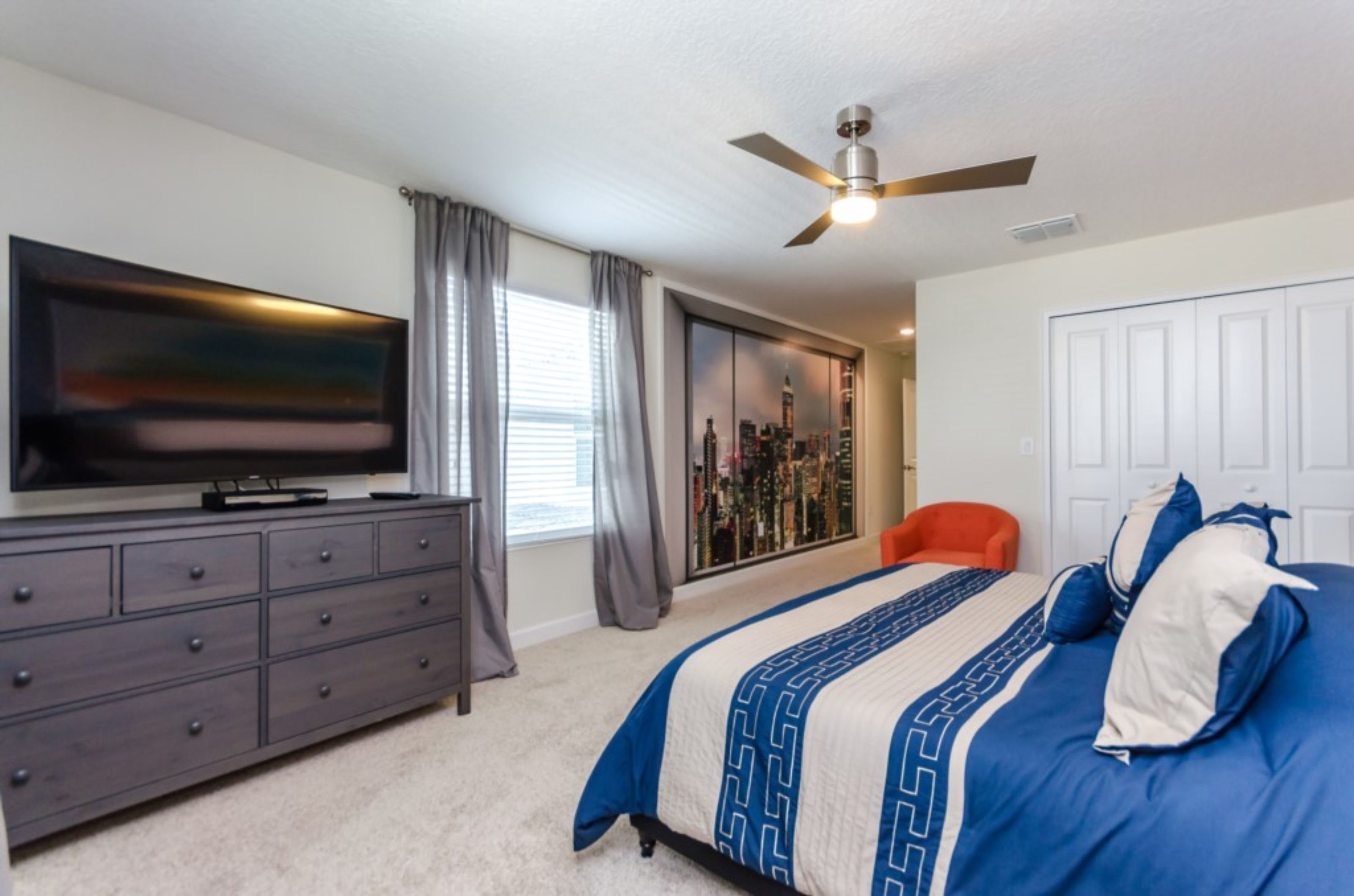 A bedroom with a bed, a TV on a dresser, a ceiling fan, and a sliding door closet.