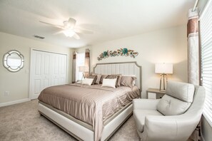 A bedroom with a bed, a chair, a ceiling fan, a decorative wall piece, and a window with curtains.