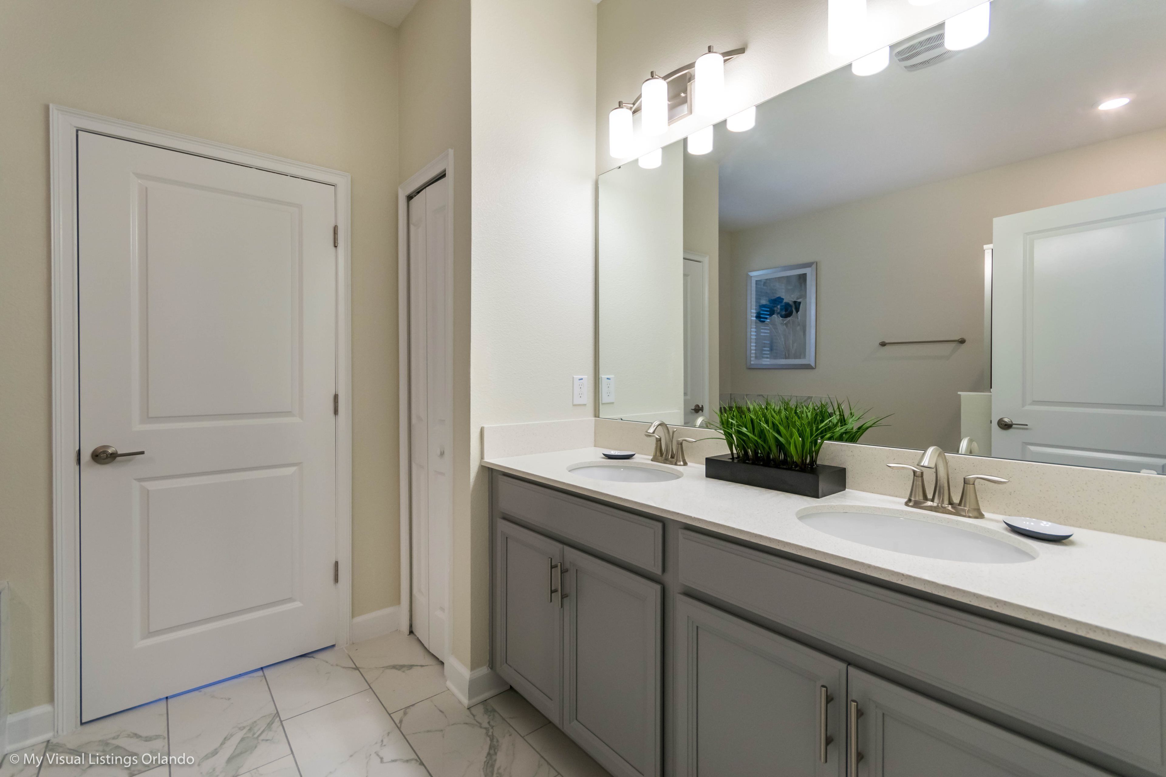 A bathroom with a double sink vanity, a large mirror, and a door.