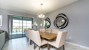 Un coin repas avec une table en bois et des chaises recouvertes d’un tissu beige, un lustre et des miroirs décoratifs sur le mur.