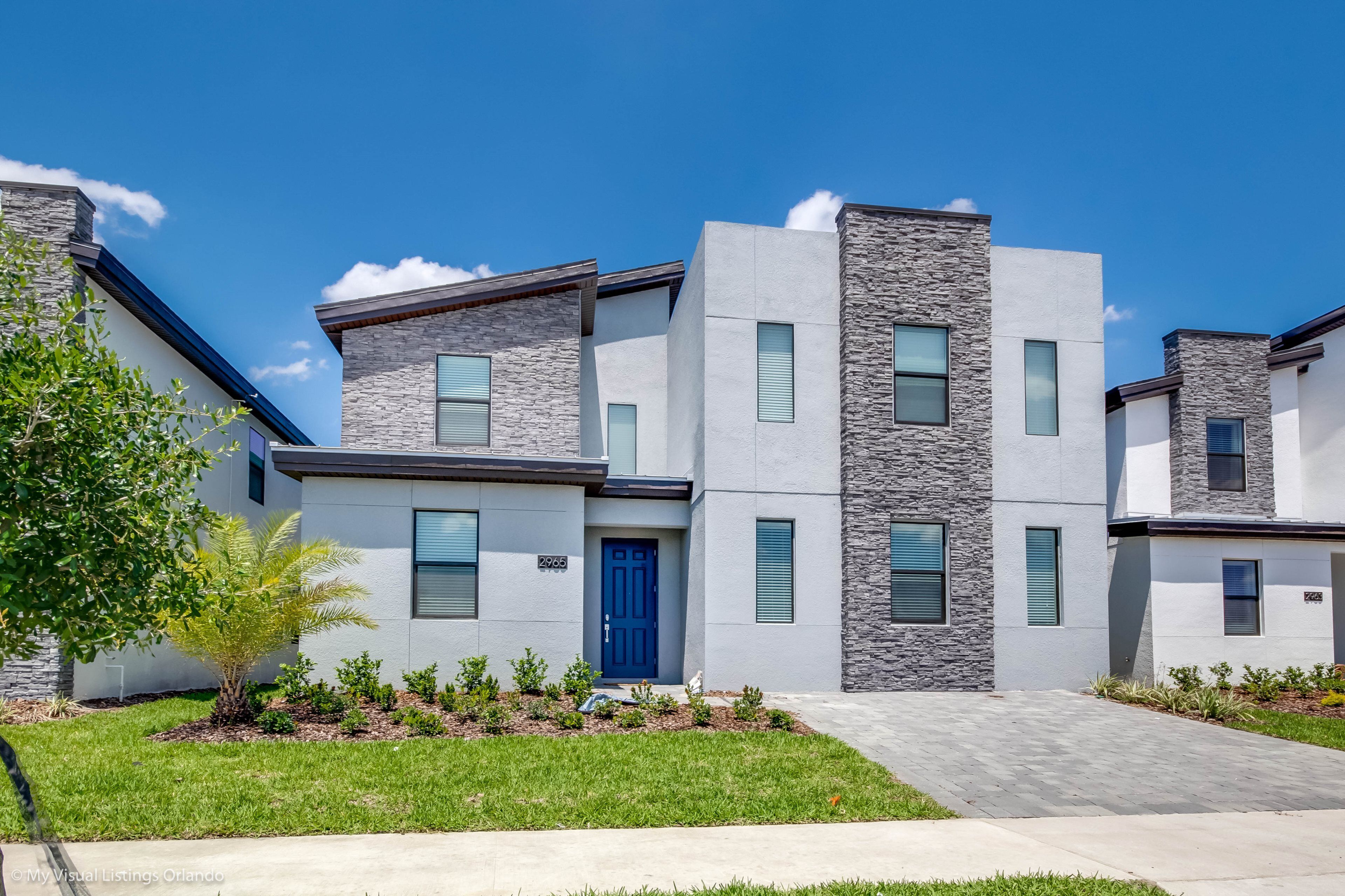 A modern two-story residential building with a blue door, stone accents, and a well-maintained lawn.