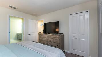 Un dormitorio con cama, cómoda, televisor y dos puertas.
