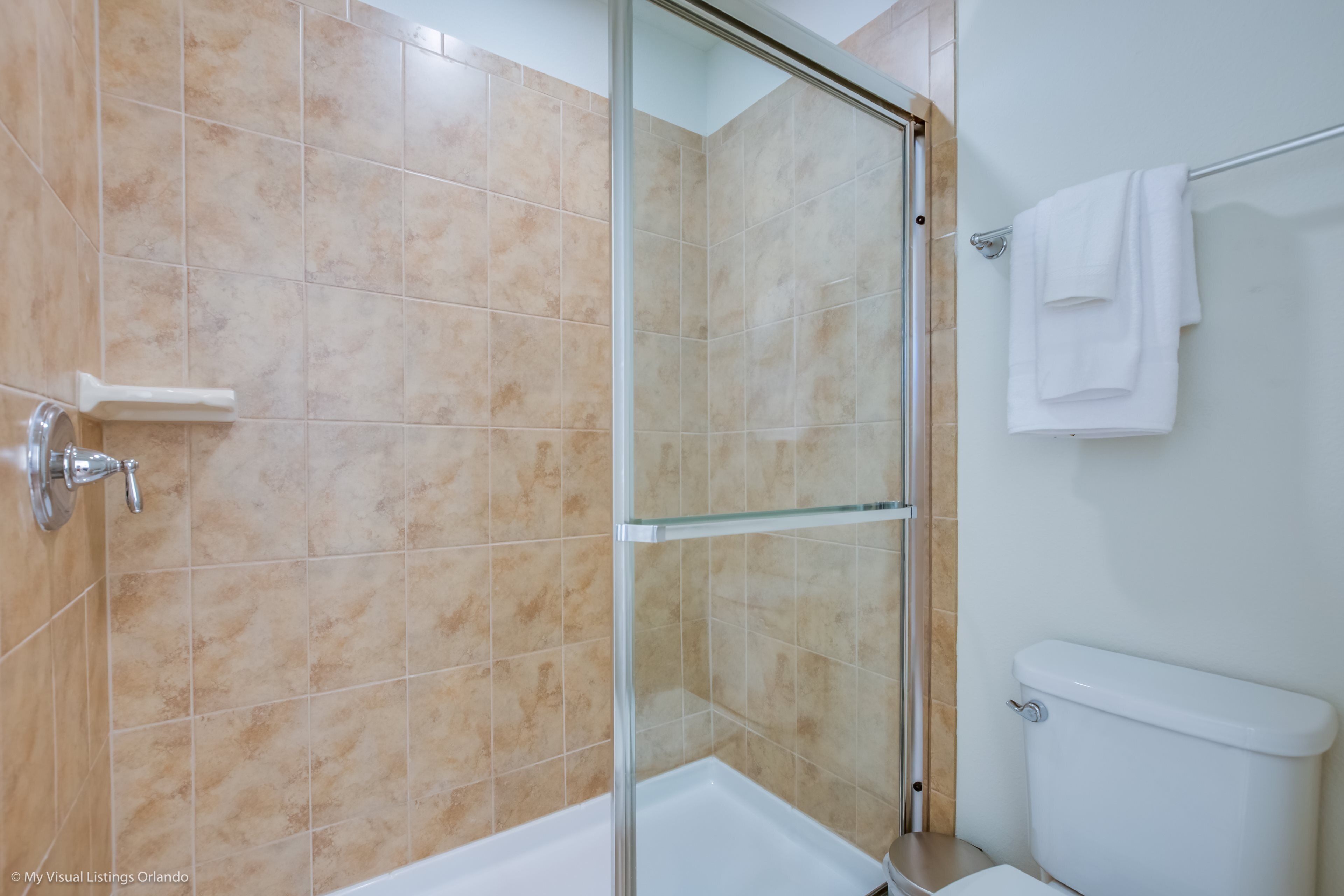 A bathroom with beige tiles, a glass shower enclosure, a white toilet, and a towel rack.