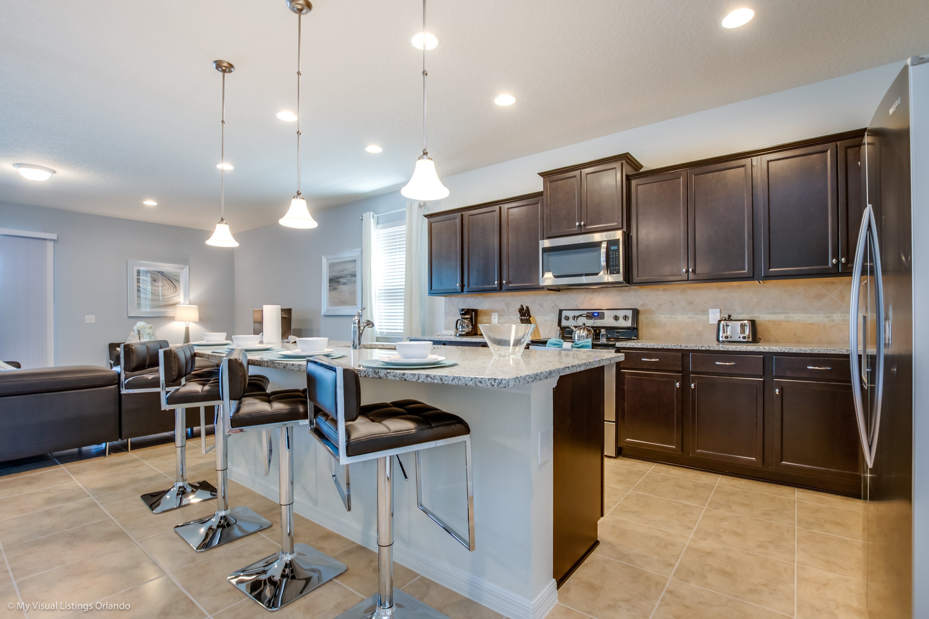 A modern kitchen with dark cabinets, stainless steel appliances, and a central island with bar stools.