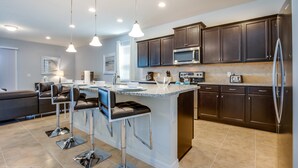 A modern kitchen with dark cabinets, stainless steel appliances, and a central island with bar stools. - 8 BD 6 BH House Villa at West Side (Kissimmee)