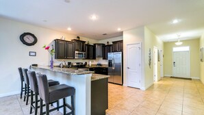 A modern kitchen with dark cabinets, a central island with bar stools, a microwave, and a refrigerator.
