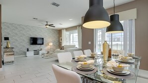 A modern dining area with a glass table set for six, surrounded by white chairs. - 6 Bed 5 Ba Villa with Games, Pool & Spa (Kissimmee)