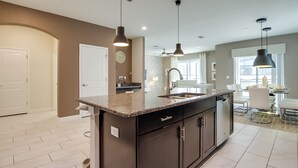 A modern kitchen with a central island, dark cabinetry, and pendant lighting. - 6 Bed 5 Ba Villa with Games, Pool & Spa (Kissimmee)