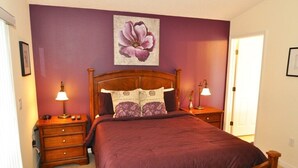 A bedroom with a wooden bed, purple walls, and a floral artwork above the bed. - Sun Lake IHR 3062 (Kissimmee)