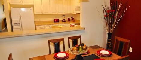 A dining area with a wooden table set for four, white cabinets, a red vase, and a vase with decorative branches.