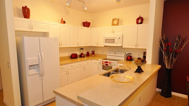 A modern kitchen with white cabinets, a refrigerator, a microwave, and a sink. - Sun Lake IHR 3062 (Kissimmee)