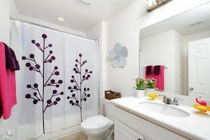 A bathroom with a shower curtain featuring a tree design, a toilet, a sink with a mirror, and a potted plant.