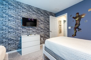 A bedroom with a brick-patterned wall, a flat-screen TV mounted above a dresser, and a bed with a white comforter.