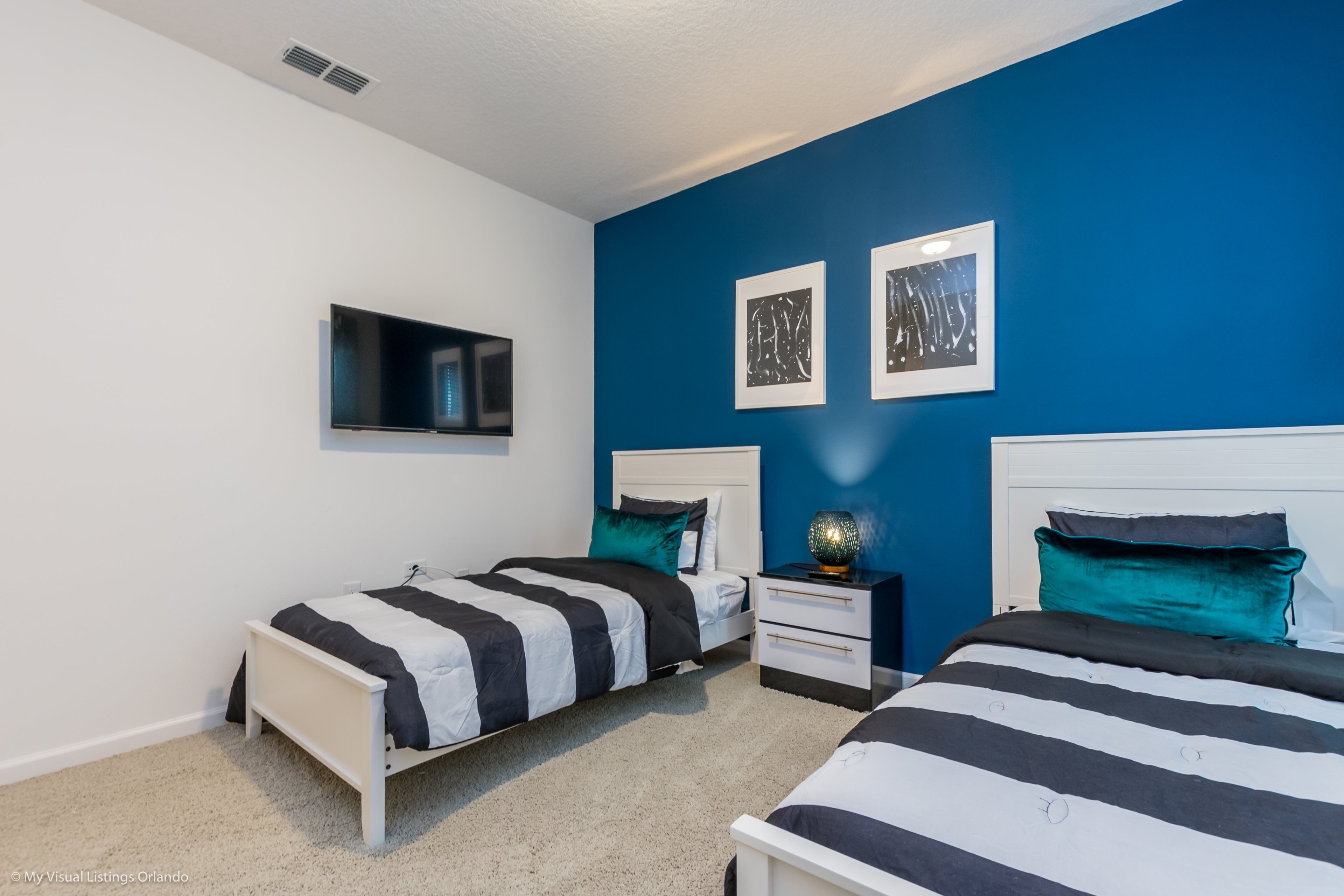 A bedroom with two beds, a white nightstand, and a wall-mounted TV.