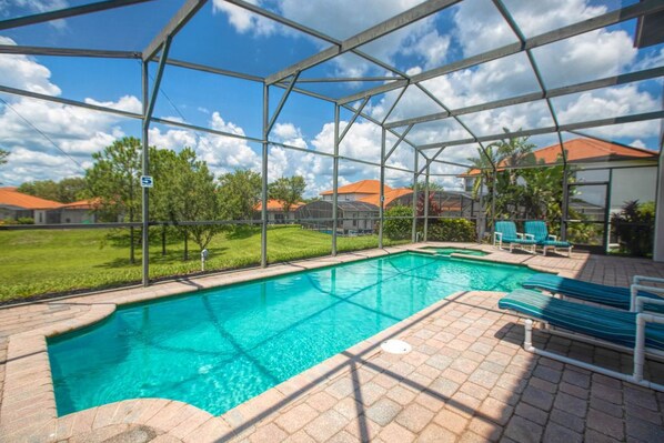 An indoor swimming pool with a clear view of the surrounding area, including a grassy lawn and buildings with orange roofs.