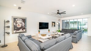 A modern living room with grey sofas, a flat-screen TV, and a large window offering a view of the outdoors.