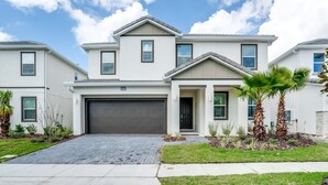 A two-story residential building with a garage, a well-maintained lawn, and palm trees.