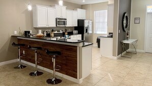 A modern kitchen with white cabinets, a central island with bar stools, stainless steel appliances, and pendant lighting. - Champions Gate - 1457gmsil (Kissimmee)