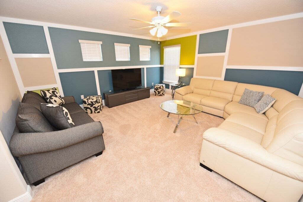 A living room with a beige sofa, a gray sofa, a glass coffee table, a TV, and a ceiling fan.