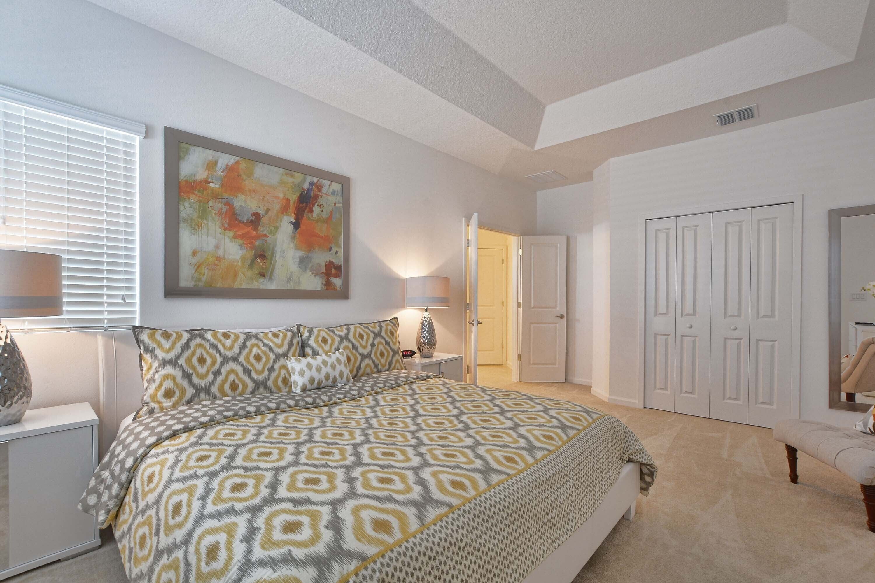A bedroom with a patterned bedspread, a bedside lamp, a nightstand, and a door leading to another room.