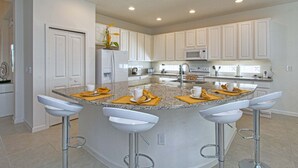 Una cocina moderna con armarios blancos, encimera de granito y una isla central con taburetes de bar.