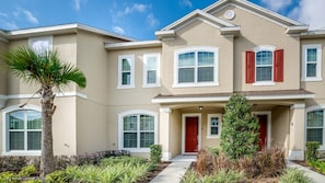 A two-story building with a beige facade, white trim, and red shutters. - Orlando Newest Resort Community Town Home (Lake Buena Vista)
