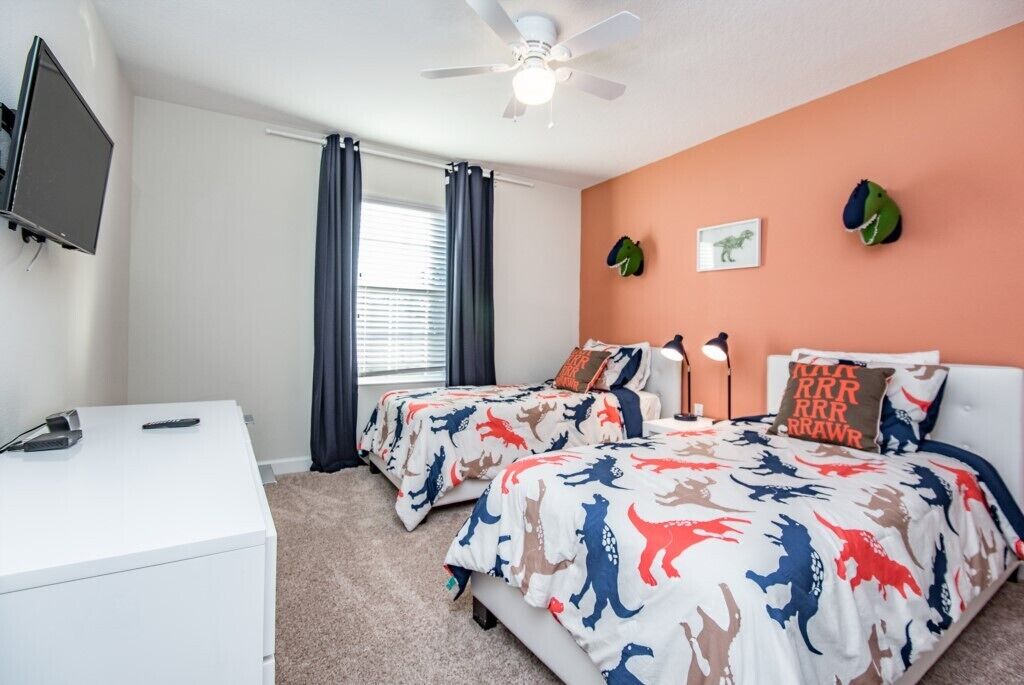 A bedroom with two beds, a desk, a ceiling fan, and a TV.