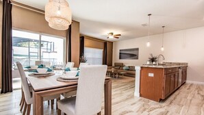 A modern kitchen with a central island, a dining area with a wooden table and chairs, and a living area with a sofa and coffee table. - 4bed 3Ba Champions Gate Pool Home (Davenport)